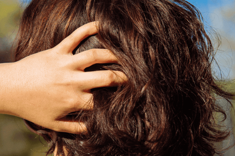 Close-up of a person’s hand running through short brown wavy hair, showing scalp and texture.