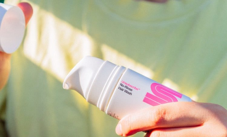 Person holding a bottle of no-rinse hair wash and removing the cap in bright natural light.