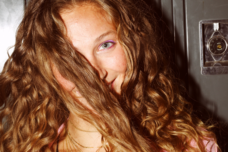 Woman with long, natural curly hair smiling with strands covering part of her face.