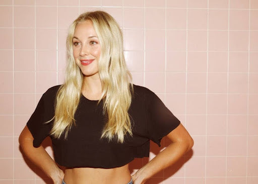 Woman smiling while standing with hands on hips in a minimalist setting.